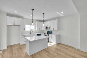 Kitchen with light countertops, a sink, light wood-style flooring, appliances with stainless steel finishes, and white cabinetry