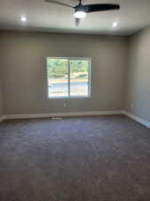 Empty room with ceiling fan, dark colored carpet, and a textured ceiling