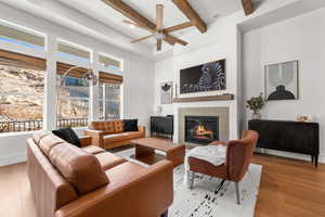 Living room featuring ceiling fan, beamed ceiling, a tile fireplace, and light hardwood / wood-style floors