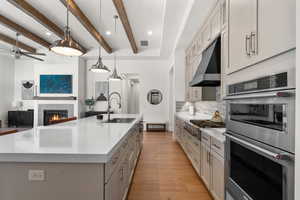 Kitchen with beamed ceiling, a large island with sink, sink, and decorative light fixtures