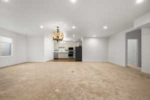 Unfurnished living room with light colored carpet, a notable chandelier, and sink