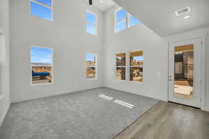 Unfurnished living room featuring light wood-type flooring, a wealth of natural light, and a towering ceiling