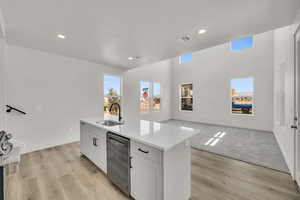 Kitchen with dishwasher, light carpet, sink, an island with sink, and white cabinetry