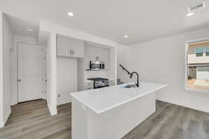 Kitchen featuring stainless steel appliances, a center island with sink, sink, tasteful backsplash, and light hardwood / wood-style flooring