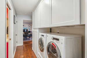 Clothes washing area with cabinets, separate washer and dryer, and dark hardwood / wood-style flooring