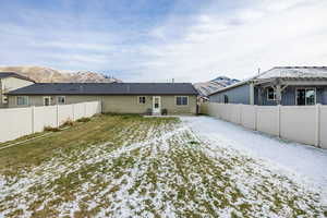 Snow covered house featuring a mountain view and a lawn