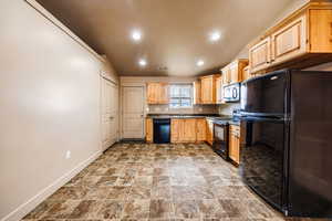 Kitchen with light brown cabinetry, sink, lofted ceiling, and black appliances