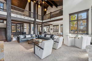 Carpeted living room with plenty of natural light, a towering ceiling, and beamed ceiling