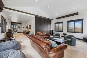 Living room with a barn door, light colored carpet, and lofted ceiling