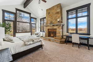 Carpeted bedroom featuring beamed ceiling, high vaulted ceiling, a stone fireplace, and ceiling fan