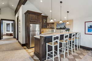 Kitchen featuring kitchen peninsula, stainless steel fridge, dark brown cabinets, pendant lighting, and a breakfast bar area