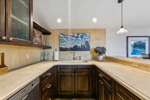 Kitchen with sink, hanging light fixtures, tasteful backsplash, stainless steel dishwasher, and vaulted ceiling