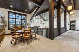 Carpeted dining space with beamed ceiling, ceiling fan with notable chandelier, high vaulted ceiling, and wood ceiling