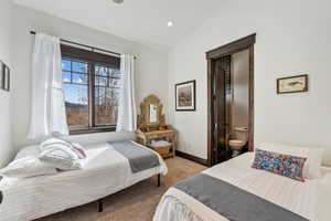 Bedroom with ensuite bathroom, carpet floors, and vaulted ceiling