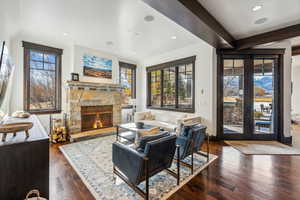 Living room with beam ceiling, a stone fireplace, and dark hardwood / wood-style floors