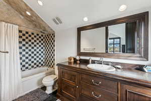 Full bathroom featuring shower / bath combination with curtain, toilet, vanity, and vaulted ceiling