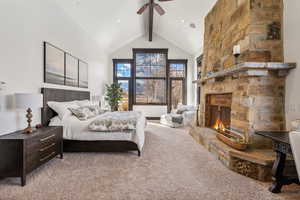 Carpeted bedroom featuring beam ceiling, high vaulted ceiling, a stone fireplace, and ceiling fan