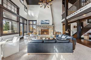 Living room featuring wood-type flooring, an inviting chandelier, high vaulted ceiling, and a stone fireplace