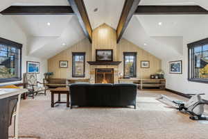 Living room with light carpet, a fireplace, lofted ceiling with beams, and wood walls