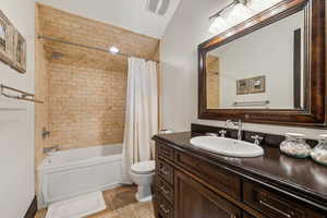 Full bathroom featuring vanity, vaulted ceiling, tile patterned flooring, toilet, and shower / tub combo with curtain