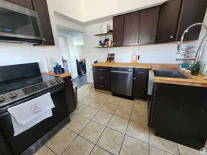 Kitchen with butcher block counters, appliances with stainless steel finishes, dark brown cabinets, and light tile patterned flooring