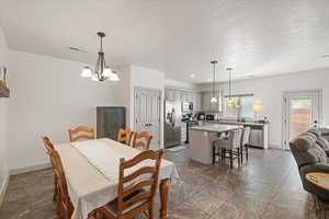 Dining area featuring sink, a textured ceiling, and a notable chandelier