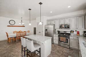 Kitchen with stainless steel appliances, light stone counters, gray cabinets, a kitchen island, and pendant lighting