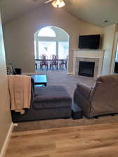 Living room featuring a tiled fireplace, light hardwood / wood-style flooring, lofted ceiling, and ceiling fan