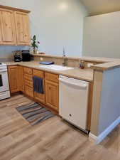 Kitchen featuring lofted ceiling, kitchen peninsula, sink, light hardwood / wood-style flooring, and white appliances
