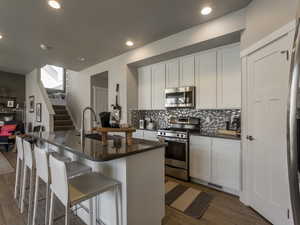 Kitchen with appliances with stainless steel finishes, dark hardwood / wood-style floors, white cabinetry, and an island with sink