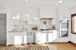 Kitchen featuring sink, light stone counters, appliances with stainless steel finishes, light hardwood / wood-style flooring, and white cabinets