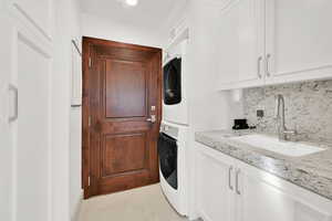 Washroom with cabinets, light tile patterned flooring, stacked washer and clothes dryer, and sink