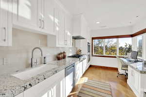 Kitchen with white cabinetry, sink, built in desk, and light stone countertops