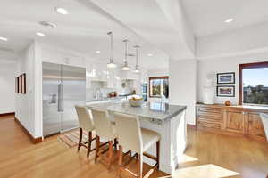 Kitchen featuring white cabinetry, appliances with stainless steel finishes, light stone countertops, decorative light fixtures, and a center island