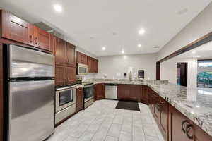 Common Area Social Room Kitchen featuring kitchen peninsula, light stone counters, and appliances with stainless steel finishes