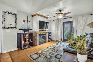 Living room with ceiling fan, wood-laminate style floors and a gas log stone fireplace,