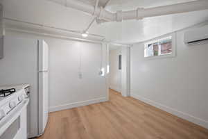 Basement featuring a wall mounted air conditioner, white fridge, and light hardwood / wood-style flooring