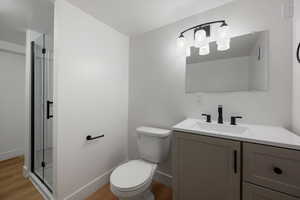 Bathroom featuring toilet, vanity, hardwood / wood-style flooring, and a shower with door