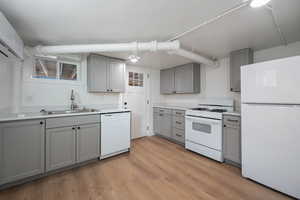 Kitchen with light hardwood / wood-style floors, sink, white appliances, and gray cabinetry