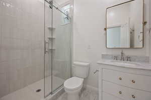 Bathroom featuring toilet, vanity, and a shower with door