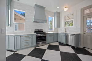 Kitchen featuring custom range hood, appliances with stainless steel finishes, sink, and a wealth of natural light