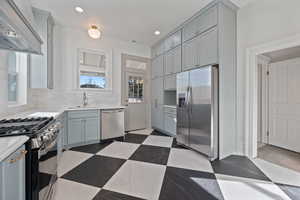 Kitchen featuring dusty blue cabinets, tasteful backsplash, premium range hood, and stainless steel appliances