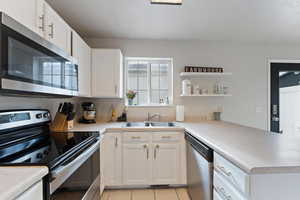 Kitchen featuring kitchen peninsula, sink, light tile patterned flooring, white cabinetry, and appliances with stainless steel finishes