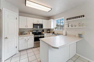 Kitchen featuring stainless steel appliances, light tile patterned floors, sink, white cabinets, and kitchen peninsula