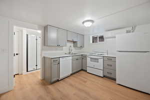 Kitchen with sink, a wall mounted air conditioner, white appliances, gray cabinetry, and light wood-type flooring