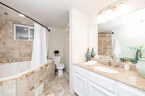 Full bathroom featuring a textured ceiling, vanity, shower / jetted bath combination with curtain, and toilet