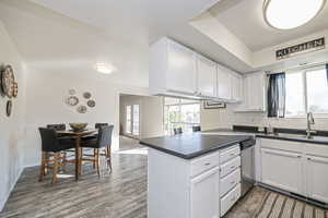 Kitchen with white cabinetry, decorative backsplash, hardwood / wood-style floors, stainless steel dishwasher, and kitchen peninsula