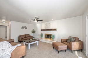 Carpeted living room featuring a textured ceiling, ceiling fan, and a brick fireplace