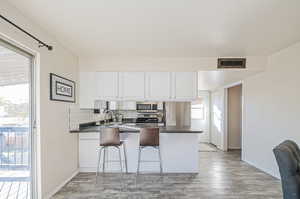 Kitchen featuring white cabinetry, appliances with stainless steel finishes, light wood-type flooring, a breakfast bar area, and kitchen peninsula