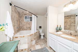 Full bathroom with toilet, shower / jetted bath combo, vanity, and a textured ceiling